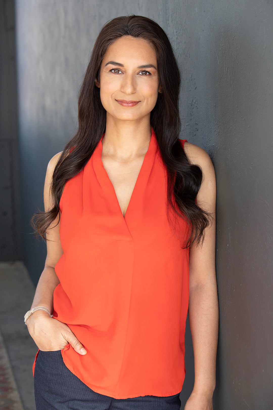 A woman standing  by the wall, her right hand on her pocket