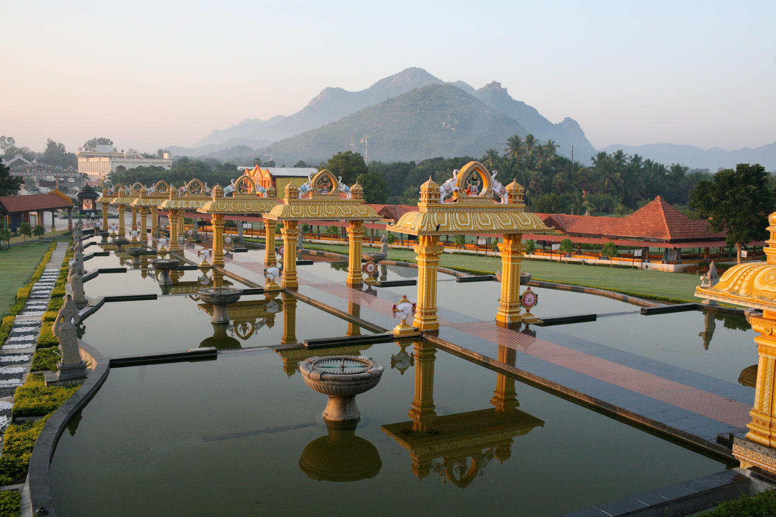 A two columned structure lines the middle with a pathway, surrounded by shallow waters with statues. Mountains in the background.