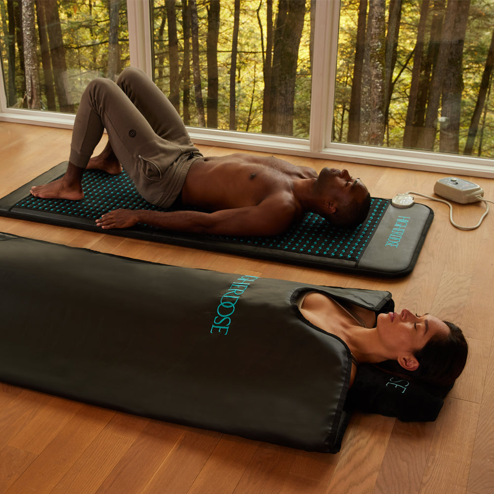 It shows 2 people using the mat indoors. The first one , with eyes closed, lying on his back, hand on the side but his feet raised with his soles to the mat and knees folded. The second person with eyes closed, is lying inside a mat but covered with a U opening in the front 