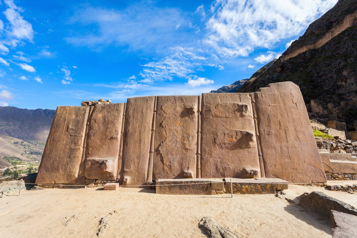 A mid shot of a big asbestos like wall, with mountains in the background and blue skies with scattered clouds