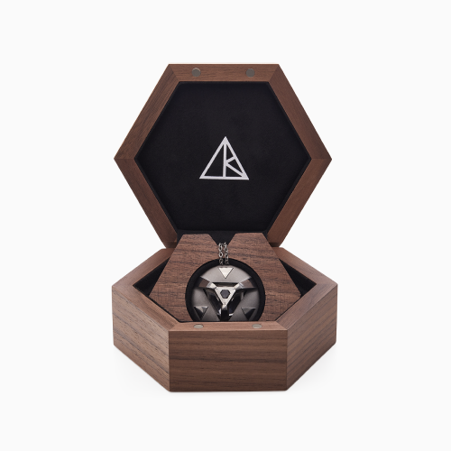 A wooden pentagon box, with its top open showing a triangular logo and inside is a circular pendant with a crystal lodged in it