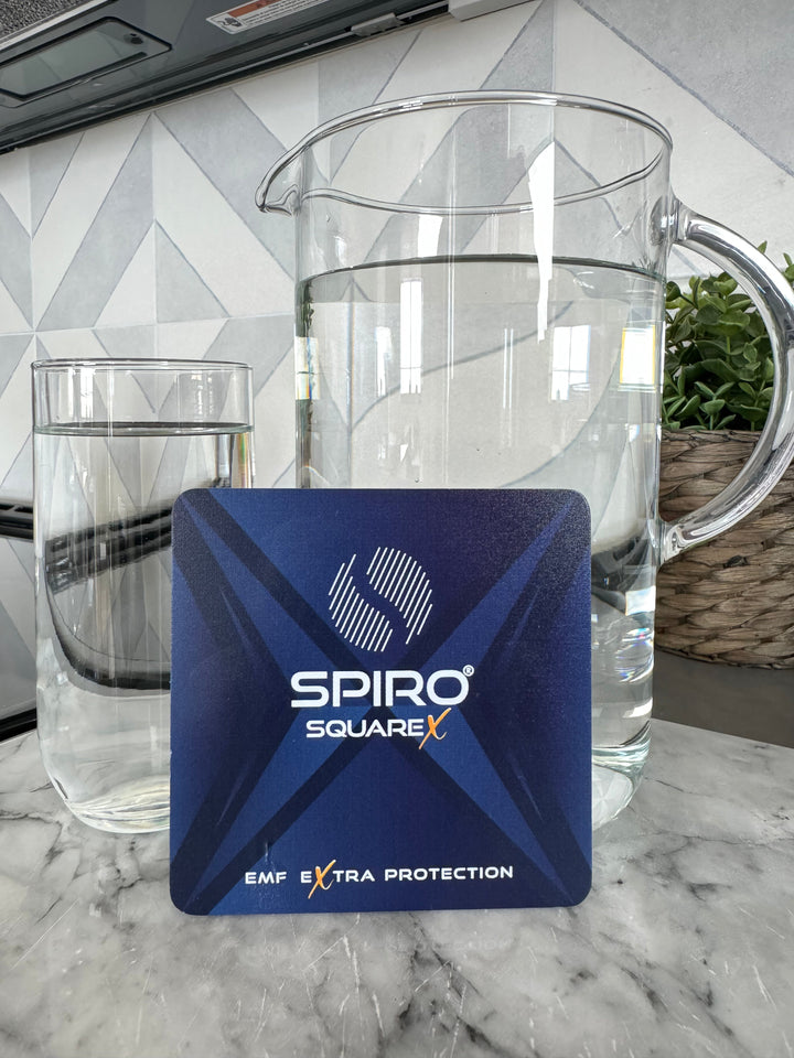 A pitcher of water and a glass of water is situated at the back of a blue square with text in the middle, Spiro square x, EMF extra protection