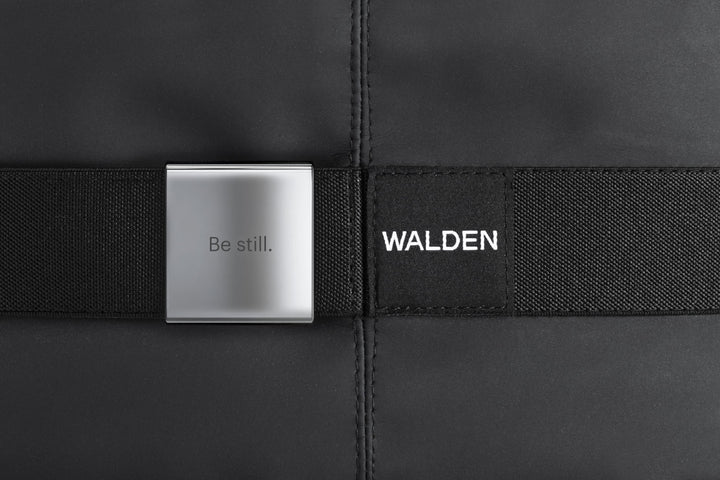 A super close up of a texted logo in a fabric that says Walden, and be still etched on a metal square chip attached in the fabric as well