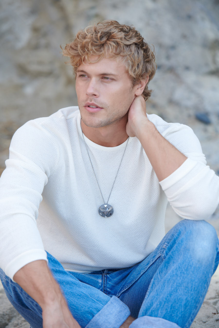 A man sitting on the ground wearing a necklace with a pendant that has a crystal lodged in it