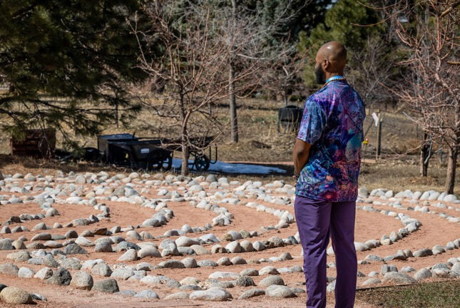 A man standing outdoors, facing a labyrinth in which the paths are outlined with small stones