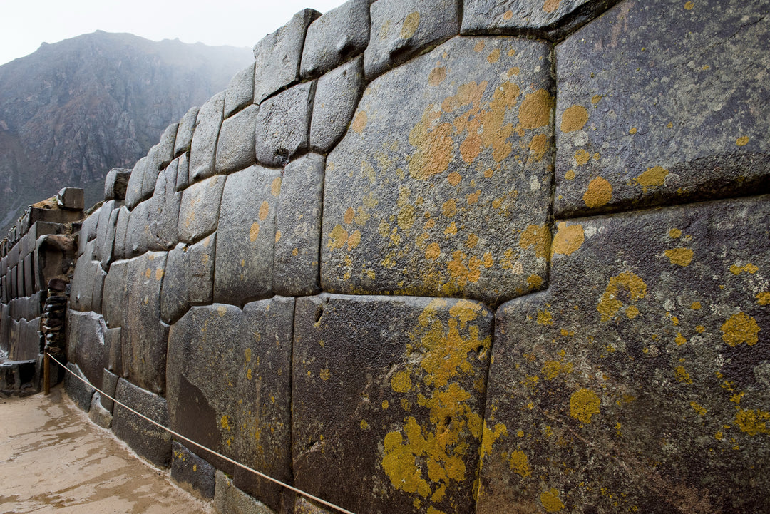 A close up of a wall built out of square-like, stacked on top of each other of dark big rocks and a mountain afar in the background