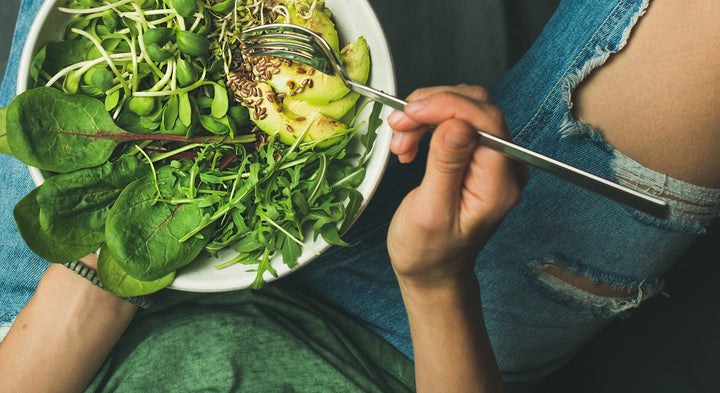 A top view of a person holding a bowl of greens on the left and a fork on the right