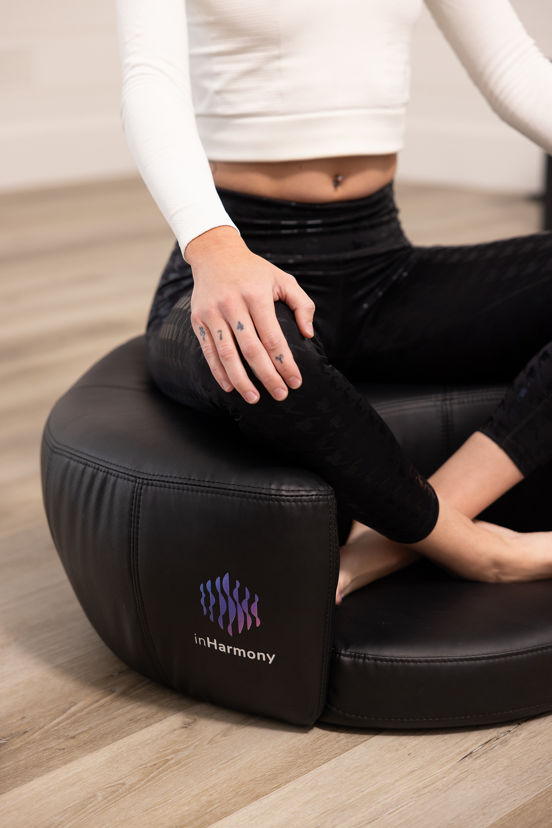 A mid-shot of a person, sitting atop a cushion with legs-crossed, and hands on the knees