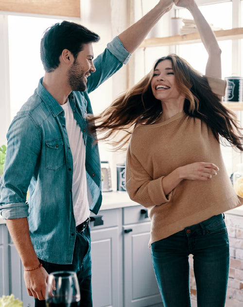 A couple in the kitchen with the man's arm upward and the woman's arm holding his hand twirling underneath