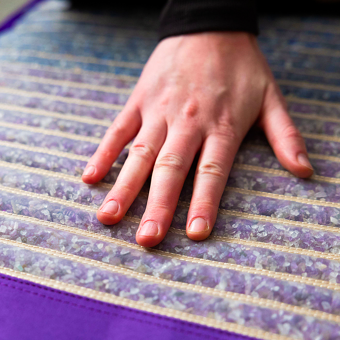 A close up of a hand touching a mat with crystals in every stitched rows