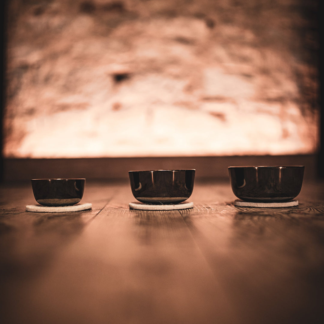 A leveled view of a three sized bowls, placed on the floor, with a cushion underneath them, with a background that's out of focus but seems to emanate light in a rocky wall