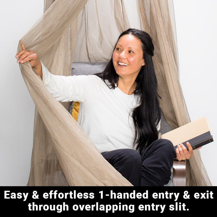 A woman sitting on a chair, smiling while holding the draped fabric from above on her right hand and a book on her left. A text below says, easy and effortless 1-handed entry and exit through overlapping entry slit.