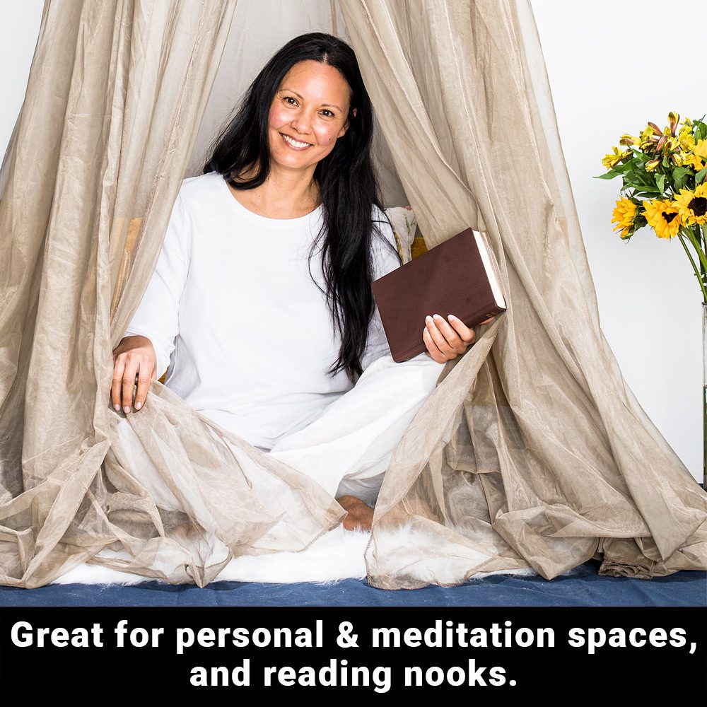 A woman sitting cross-legged on the floor, smiling to the camera while holding a book on her left hand, draped with a fabric over head that hangs above. A text below says, great for personal and meditation spaces, and reading nooks.