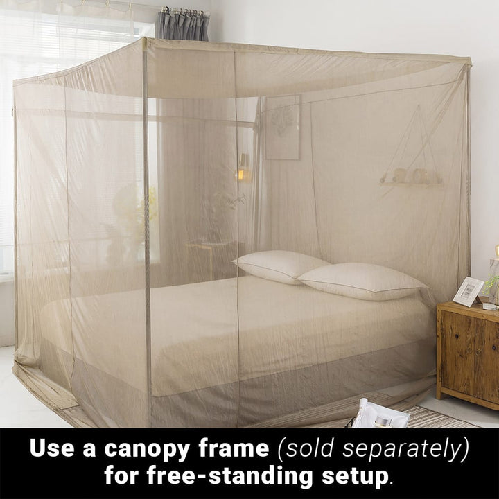 A diagonal view of a bed with pillows covered with a canopy squared fram of fabric with a text below, use a canopy frame (sold separately) for free-standing setup.